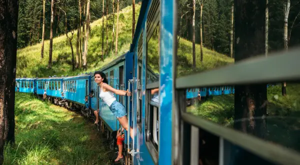 Pociąg Sri Lanka mknie przez zielone wzgórza. Kobieta wychyla się z okna, ciesząc się widokiem.