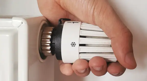 Regolare valvole termostatiche stanza per stanza: mano che gira la manopola del termosifone per impostare la temperatura desiderata.