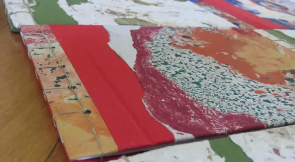 Dettaglio di come rilegare fogli a mano con filo, creando un quaderno artistico con copertina colorata.