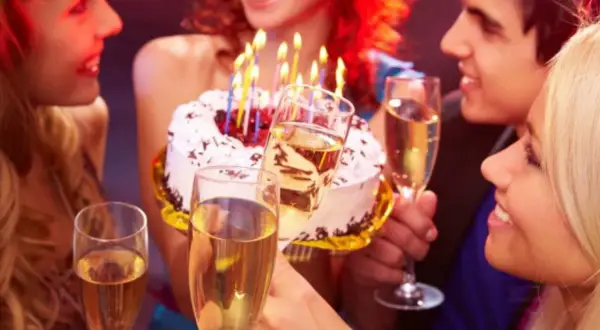Amigos celebran con pastel y copas de champán. ¡Así se escribe happy birthday en español: ¡Feliz Cumpleaños!