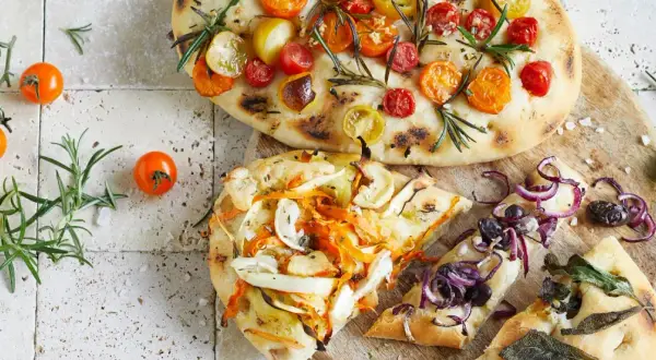 Zwei Focaccias mit Tomaten, Gemüse und Zwiebeln, garniert mit Rosmarin und Salbei.