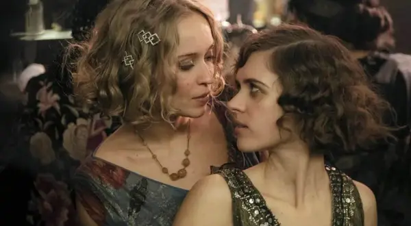Zwei Frauen im Stil der 1920er Jahre, eine mit blonden Locken und Schmuck, die andere mit dunklen Locken, blicken sich intensiv an. Ein Moment aus Babylon Berlin Staffel 5.