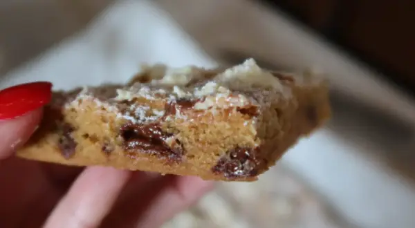 En hand håller en bit av ett blondie recept med chokladbitar.