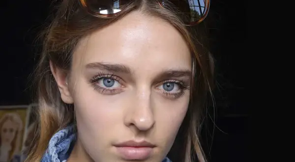 Ragazza con occhiali da sole in testa, viso illuminato da fondotinta e fard, ciglia lunghe e occhi azzurri.
