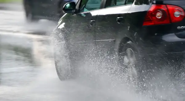 Un coche negro salpica agua al pasar por un charco. En días de lluvia, una distancia de frenado segura depende de la precaución.