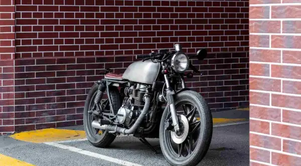 Stylowy motocykl miejski z metalicznym bakiem i brązowym siedzeniem stoi przy ceglanej ścianie.