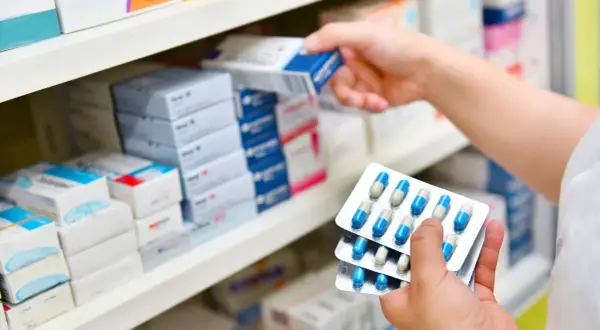 Ręka farmaceuty wybiera z półki lek, w tym antybiotyk azytromycyna w blistrach.