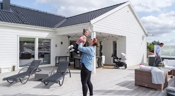 En kvinna lyfter sitt barn på en altan vid ett modernt hus, en idyllisk semesterbild från ett resort i Sverige.