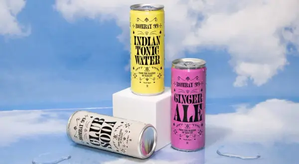 Three Bombay 99+ cans: Club Soda, Indian Tonic Water, and Ginger Ale, styled by Jessica Walsh, against a sky backdrop.