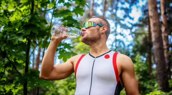 Mężczyzna w sportowym stroju pije wodę z butelki, co pić podczas treningu w plenerze.