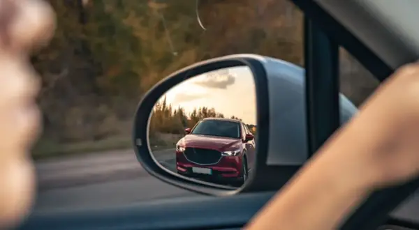 Reflejo de un coche rojo en el espejo retrovisor, preparándose para un adelantamiento. DGT.