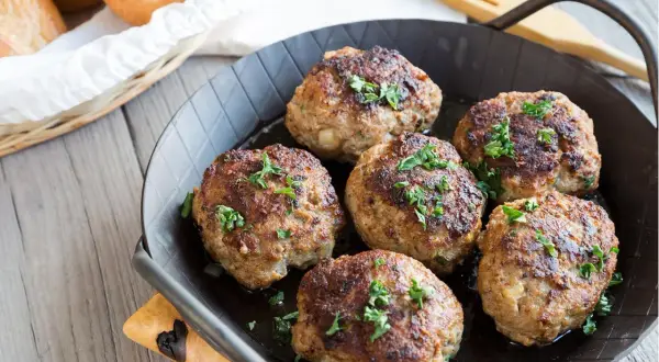 Sechs goldbraune Fleischpflanzerl, frisch aus der Pfanne, garniert mit Petersilie. Ein leckeres Fleischpflanzerl Rezept zum Nachkochen.