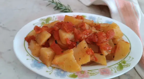 Patate in umido con pomodoro e rosmarino, un piatto semplice e gustoso, servito su un piatto fiorato.