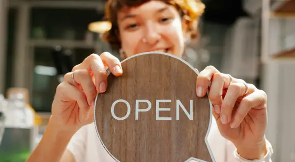 Frau hält ein Holzschild mit der Aufschrift "OPEN" in einem Café.
