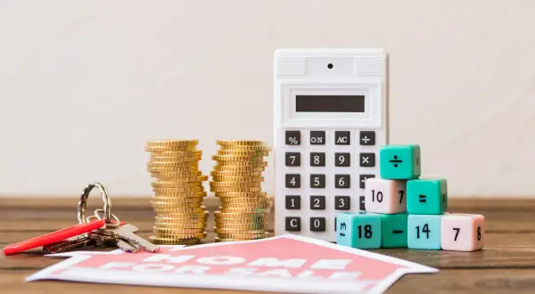 Calculadora, monedas y llaves junto a dados con números y símbolos matemáticos, sugiriendo el cálculo del valor de mercado de un inmueble.