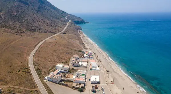 Vista aérea de la playa de la Almadraba en Almería, con el mar azul intenso, la arena dorada y un pueblo costero.