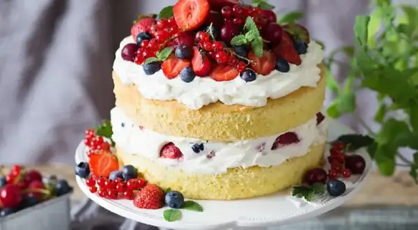 Puszysty tort z bitą śmietaną i mascarpone, ozdobiony świeżymi truskawkami, borówkami i porzeczkami. Idealny na letnie przyjęcie.