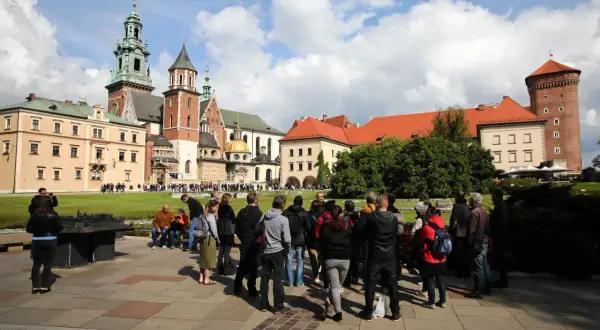 Grupa turystów zwiedza Wawel. Sprawdzają wawel bilety cennik przed wejściem.