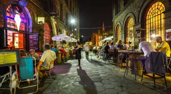 Wieczór na ul. Piotrkowskiej w Łodzi. Ludzie siedzą przy stolikach w restauracjach, ciesząc się atmosferą.