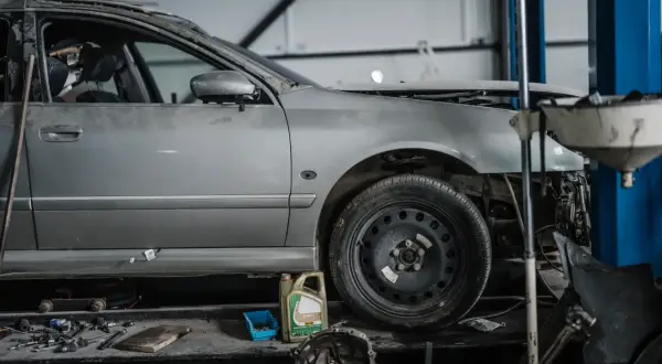 Voiture argentée en réparation dans un garage, avec des outils et une boîte d'huile. Le frein à main est prêt pour le prochain contrôle.