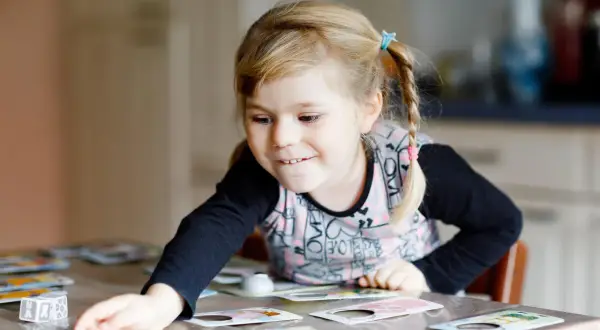 Niña rubia con coletas jugando a un juego de memoria infantil, concentrada en las cartas sobre la mesa.