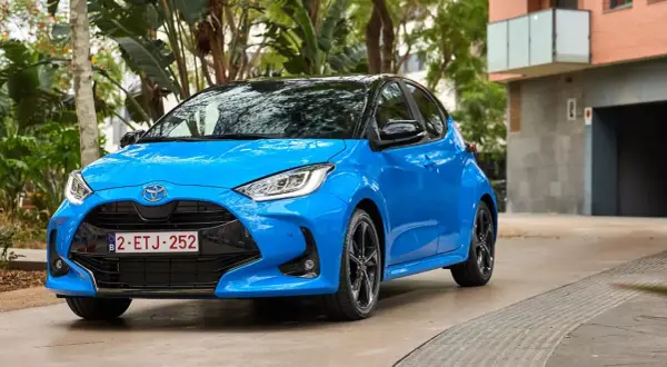 Błękitna Toyota Yaris 1.3 benzyna zaparkowana na tle zieleni i budynku. Zastanawiasz się, jaki olej do toyoty yaris 1.3 benzyna?