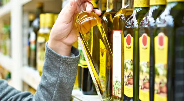 Ręka wybiera butelkę oliwy z oliwek. Czy oliwa z oliwek może zamarznąć? Niska temperatura może spowodować jej zmętnienie, ale nie zepsuje jej.