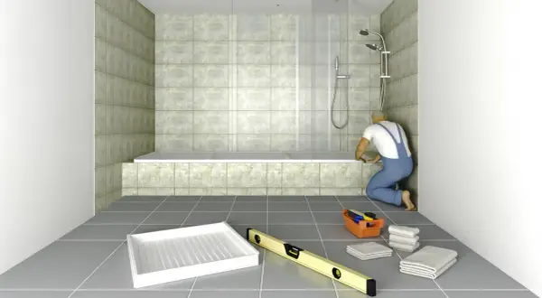 Un obrero instala una bañera de obra. Herramientas y toallas esperan en el suelo.