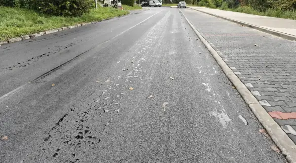 Droga w Cieszynie po deszczu, z kałużami na asfalcie i nowym chodnikiem z kostki.