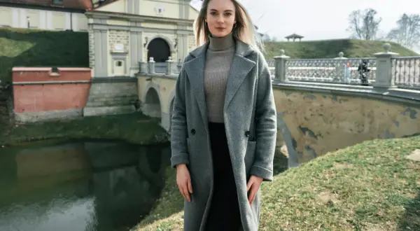 Kobieta w szarym płaszczu i golfie, idealna stylizacja na 14 stopni. W tle zamek i fosą.