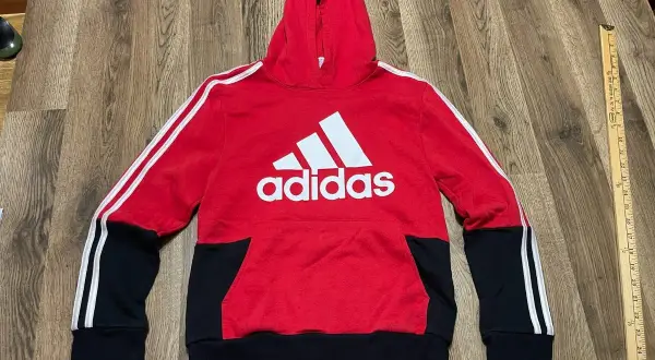 Czerwona bluza z kapturem Adidas dla chłopca z białym logo i czarnymi wstawkami.