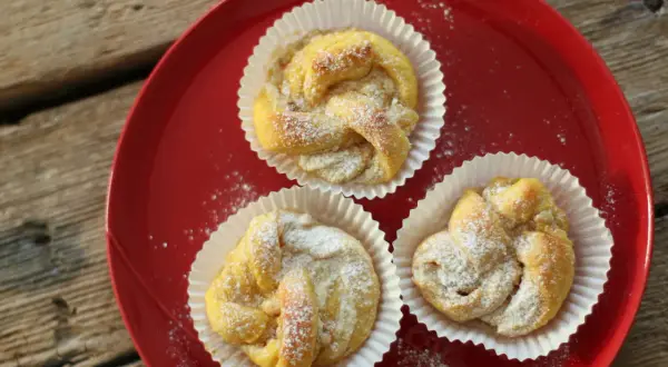 Tre små bakverk med saffran och vit choklad, pudrade med florsocker, ligger på en röd tallrik.