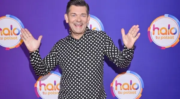 Zenek Martyniuk w czarno-białej koszuli w grochy, z podniesionymi rękami, na tle fioletowym z logo "halo tu Polsat".