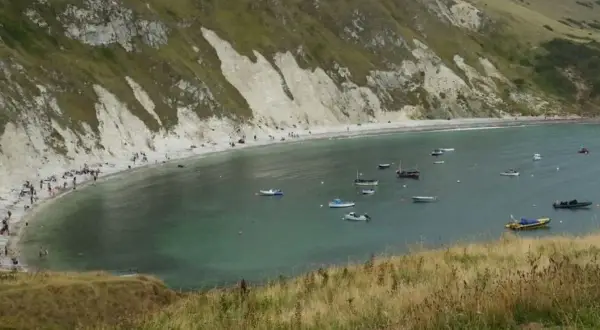 Malownicze morze w Anglii, zatoka pełna łodzi, z plażą i ludźmi w oddali.