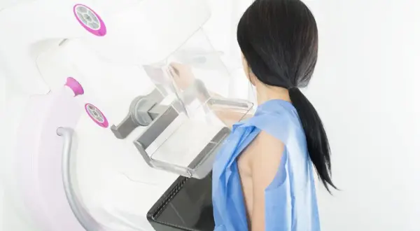 Kobieta w niebieskiej koszuli przygotowuje się do mammografii. Badanie jest ważne, choć czasem mogą wystąpić powikłania po mammografii.