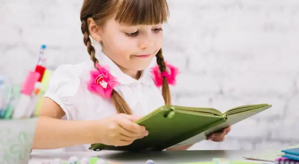 Dziewczynka z warkoczami czyta książkę, marząc o przyszłości, gdy zdobędzie kurs pedagogiczny uprawniający do pracy w szkole.