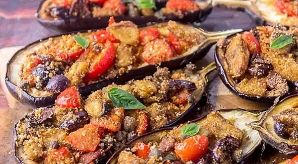 Melanzane a scarpone ripiene di pomodoro, olive e pangrattato, guarnite con basilico fresco. Un piatto saporito e invitante.