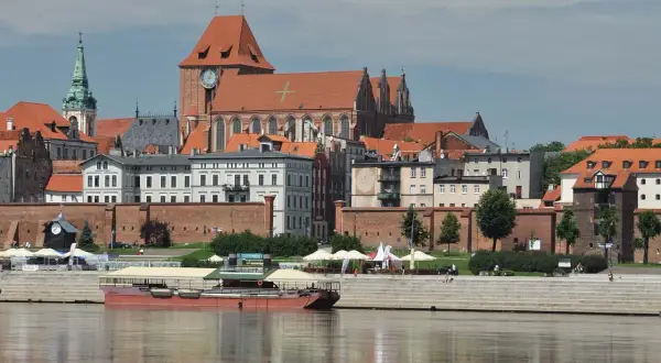 Widok na średniowieczny zespół miejski Torunia z Wisłą w tle. Zabytkowe kamienice i kościół tworzą malowniczą panoramę.