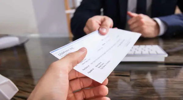 Mancata riscossione di assegno bancario dopo rogito notarile. Mano che porge un assegno, con un uomo in giacca e cravatta sullo sfondo.