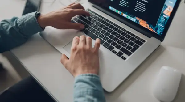 Osoba pracuje na laptopie, planując podróż z mbank konto wielowalutowe. Na biurku leży też myszka i telefon.