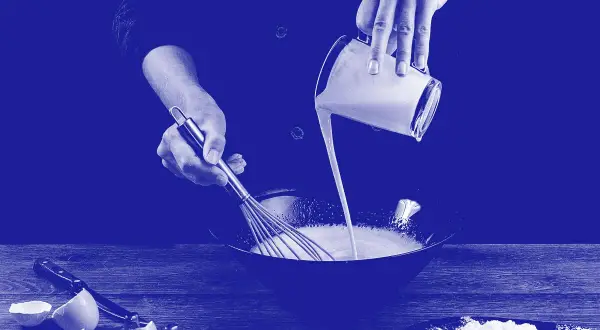 Manos mezclando diferentes tipos de leche en un bol. Huevos rotos y harina en la mesa.