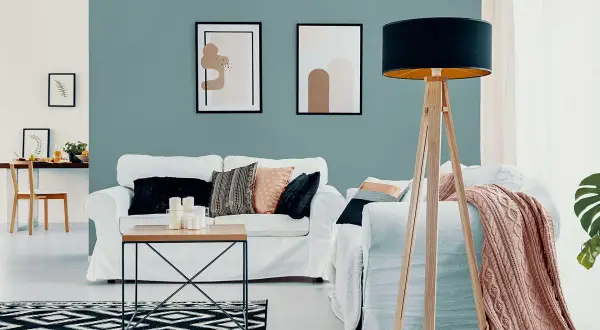 Nowoczesny salon z białymi sofami, stolikiem kawowym i lampą na drewnianym statywie. Ściana w odcieniu **kolor lazurowy** tworzy spokojną atmosferę.