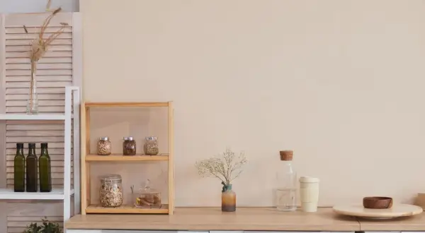Regale mit Vorräten, Ölflaschen und Pflanzen zeigen **minimalismus im alltag**. Eine Vase mit Trockenblumen und eine Wasserflasche ergänzen die Szene.