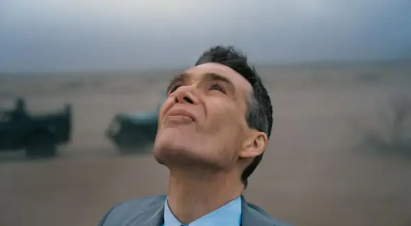 Oppenheimer patrzy w niebo, w tle mglisty krajobraz z pojazdami.