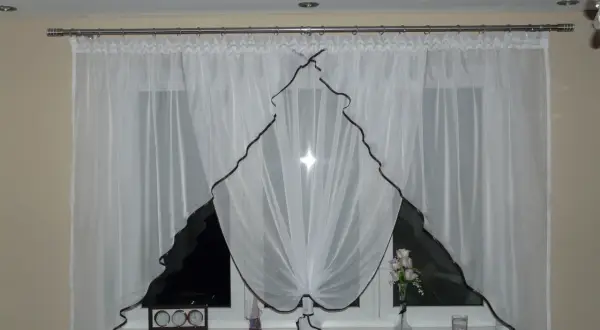Eleganckie białe firanki z brązową lamówką, idealnie pasujące na karnisz 2m. Na parapecie zegar i wazon z kwiatami.