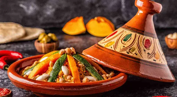 Un saporito cous cous tajine con verdure colorate e ceci, servito in un tradizionale piatto di terracotta decorato.