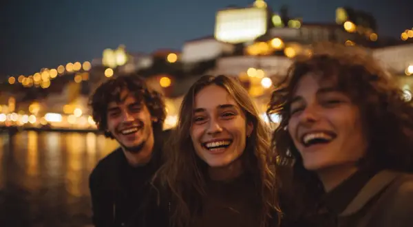 Tre amici ridono felici, immersi nella magica atmosfera del porto vita notturna, con le luci sfocate della città a fare da sfondo.