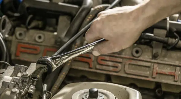 Ręka mechanika używa klucza motylkowego do dokręcania śruby w silniku Porsche.