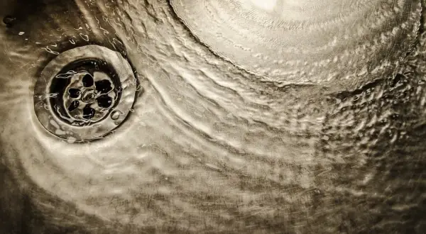 Acqua che scorre su uno scarico metallico, un'immagine che evoca il processo di come sciogliere il grasso nei tubi di scarico.