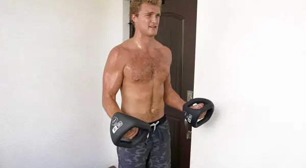 A muscular man with sweaty boxer forearms holds two black dumbbells, ready for a workout.